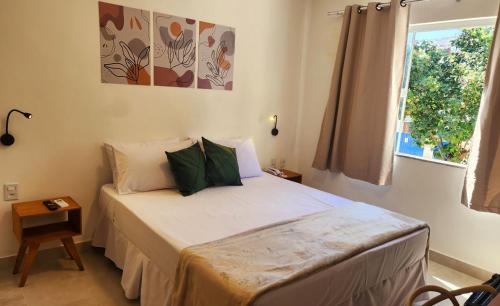 a bedroom with a bed with white sheets and green pillows at Pousada Noa in Cabo Frio