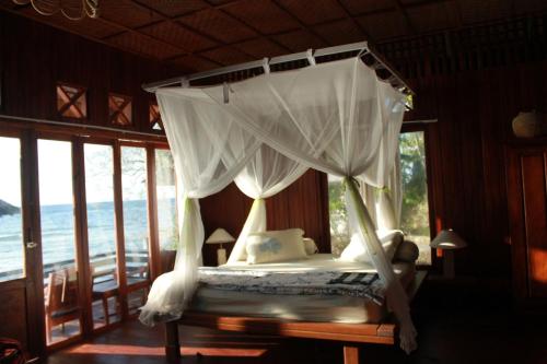 a bedroom with a canopy bed with a view of the ocean at Kadidiri Paradise in Batudaka
