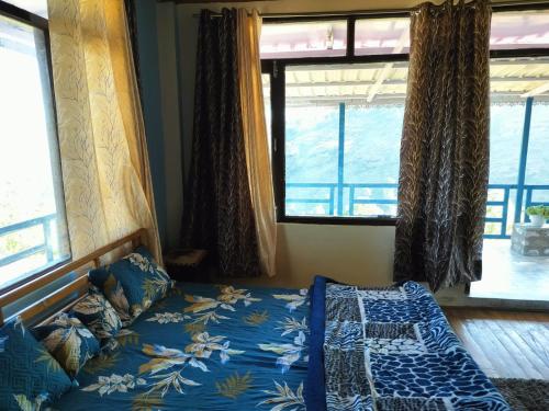 a bedroom with a bed with blue sheets and windows at Nirvana Heights Kasar Devi in Hawālbāgh