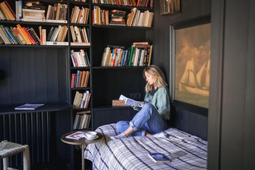 a woman sitting on a bed reading a book at Hôtel Lilybloom in Le Havre