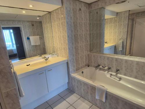 a bathroom with a sink and a tub and a mirror at Dolphin Beach Hotel Self Catering Apartments in Bloubergstrand