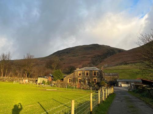 an old house in a field with a hill in the background at Stybeck Farm in Thirlmere