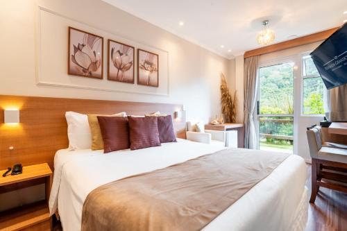 a bedroom with a large white bed and a window at Pousada Grandchamp - Campos do Jordao in Campos do Jordão