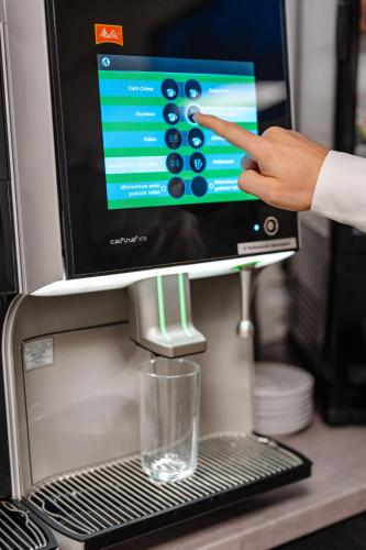 a person pointing at a coffee machine with a glass at Sonnenschein Hotel & Apartments in Heilbad Heiligenstadt