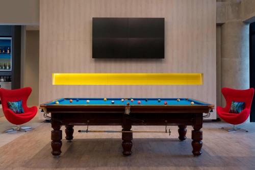 a pool table in a room with red chairs and a tv at Aloft Jakarta Wahid Hasyim in Jakarta