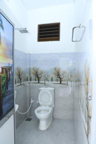 a bathroom with a toilet with a painting on the wall at 19 Southern Homestay in Dickwella