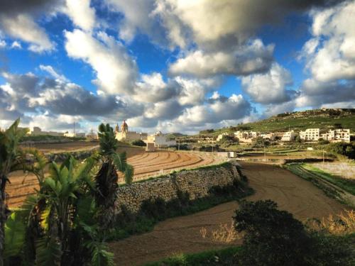 uma vista para um campo com casas e um céu nublado em Farmhouse Dhyana em Għasri