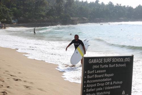 a man holding a surfboard next to a sign on the beach at Muru's Place in Dickwella