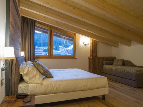 a bedroom with a bed and a couch and windows at Hotel Garnì Caminetto in Madonna di Campiglio