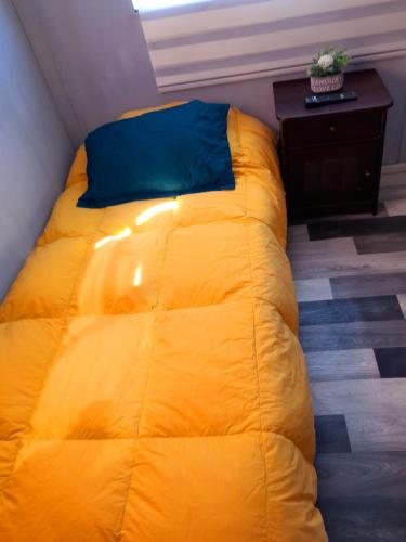 a yellow bed with a blue pillow and a table at Casa familiar in Punta Arenas