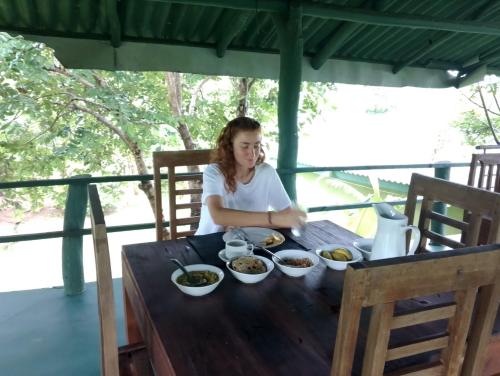 a woman sitting at a wooden table with food at Sigiri Prabha Villa in Sigiriya