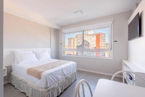 a white bedroom with a bed and a window at Connect by LikeHome in Porto Alegre