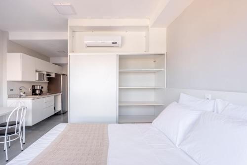 a white bedroom with a bed and a kitchen at Connect by LikeHome in Porto Alegre