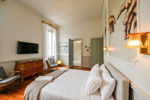 une chambre avec un lit blanc et une télévision dans l'établissement DE L'ART À LA MANIÈRE - Chambre d'Hôtes de Charme - 2 Suites Haut de Gamme - Idéal Couple & Famille - Piscine - Terrasse - Calme - 15min Saint-Émilion - EXPÉRIENCE Restauration d'Oeuvre d'Art, à Branne