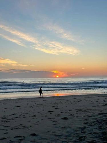 una persona caminando por la playa al atardecer en Située a 3 minutes de la plage, en Yof