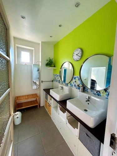 La salle de bains est pourvue de 2 lavabos et d'un mur vert. dans l'établissement La Maison Cardau, à Névian