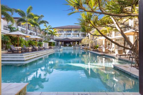 a swimming pool in a resort with palm trees and buildings at Santai Resort - Holiday Management in Kingscliff