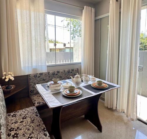 a table with plates and cups on it in front of a window at Flet dos sonhos in Florianópolis