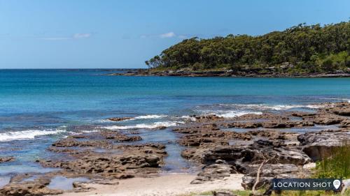 a beach with rocks and the ocean and trees at Sea Bubbles in Currarong