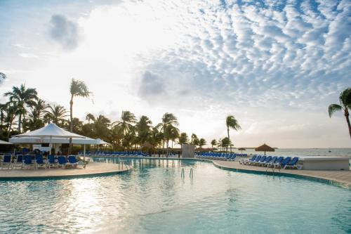 a pool at the beach with chairs and palm trees at Renaissance Wind Creek Aruba Resort in Oranjestad
