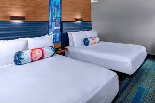 ローリーにあるAloft Raleigh Durham Airport Brier Creekの白いシーツと枕が備わったホテルの部屋にはベッドが2つある
