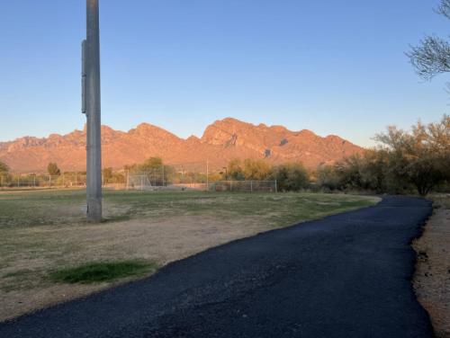 a road leading to a field with mountains in the background at Private Home - Billiards, Mountain Views, Private Desert Access, HOA Pool & Spa, BBQ, at Lambert Park - Bourbondale in Tucson