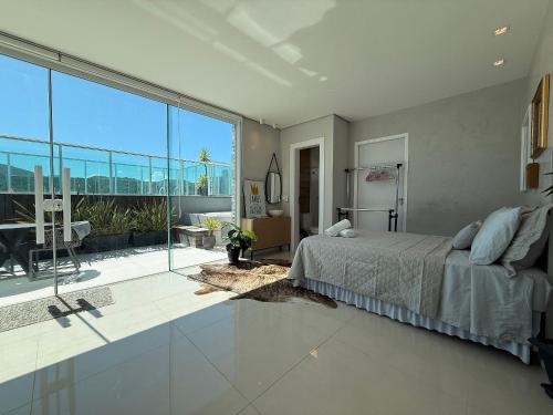 a bedroom with a bed and a large window at QE01- Studio| Jacuzzi Aquecida| Piscina| Churrasq. in Cabeçudas