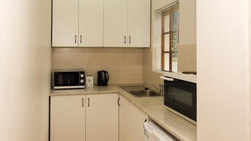a kitchen with white cabinets and a sink and a microwave at 39 On Nile Guest House in Port Elizabeth