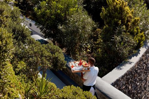 a man holding a tray of food in a garden at San Antonio - Small Luxury Hotels of the World in Imerovigli