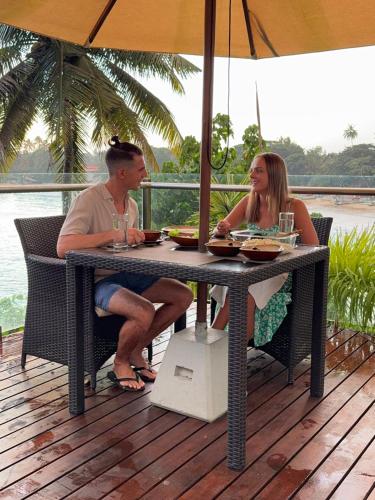 a man and woman sitting at a table under an umbrella at Beacon By The Bay Villas and Suites by the Clarks in Matara