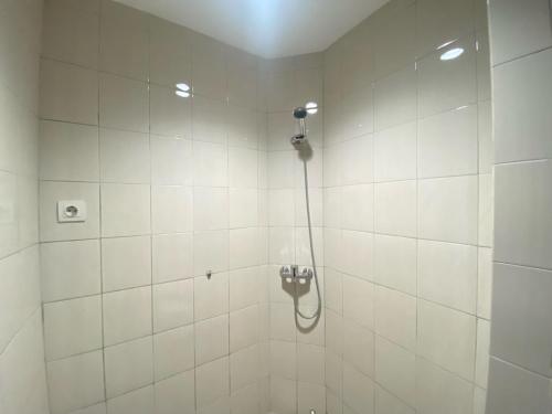 a shower with a hose in a white tiled bathroom at Bright and Relaxing 2BR Apartment at Mekarwangi Square Cibaduyut By Travelio in Bandung