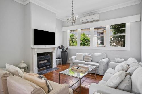 a living room with white furniture and a tv at Charming House in Woolwich in Sydney