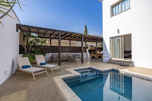 a swimming pool with two chairs and a table and a house at Agios Tychon Luxury Villa with Private Pool in Limassol