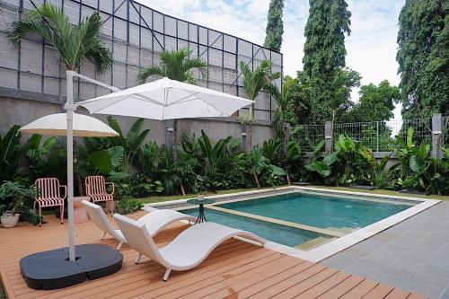 a swimming pool with two chairs and an umbrella and a table and chairs at Ponder Bali Canggu in Canggu