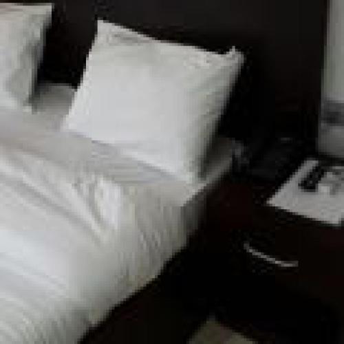 a bed with white sheets and a pillow next to a nightstand at Habitat Hotel and Suites -Standard in Port Harcourt