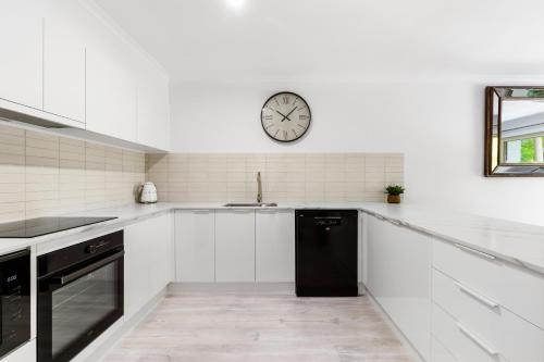 a kitchen with white cabinets and a clock on the wall at Elvis - The Great Seaside Escape - Luxury Stay in Coffs Harbour