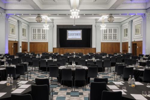 a large room with tables and chairs in front of a screen at Kimpton Clocktower by IHG in Manchester