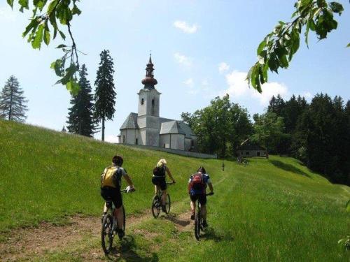three people riding bikes down a hill in front of a church at Apartmaji Koželj in Ribnica na Pohorju