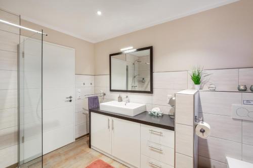 a white bathroom with a sink and a mirror at Wellnes Bungalow Sanddüne in Fehmarn