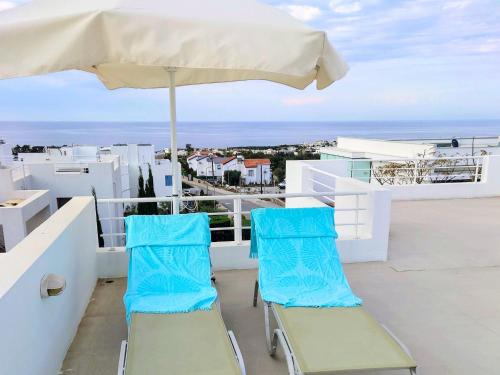 two chairs and an umbrella on a balcony with the ocean at Penthouse Apartment with Stunning Sea and Mountain Views in Ayios Yeoryios