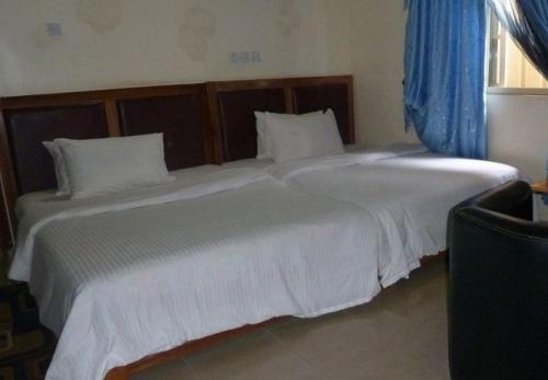 a bedroom with two large white beds with blue curtains at Definite Destiny Hotel - Standard in Asaba