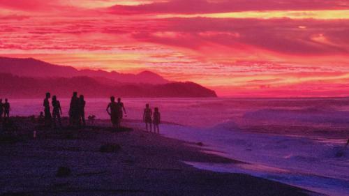 a group of people standing on a beach at sunset at Blue Mango Beach Hotel in Guachaca