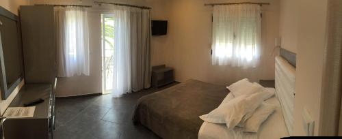 a bedroom with a bed and a television and windows at Vournelis Beach Hotel and Spa in Iraklitsa