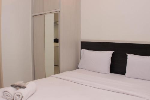 a bedroom with a bed with white sheets and a mirror at Cozy Living Studio at Urbantown Apartment Karawang By Travelio in Karawang