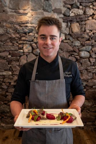 a man in an apron holding a plate of food at Hotel Al Lago in Soraga