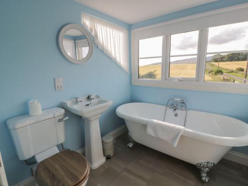 La salle de bains est pourvue d'une baignoire blanche, d'un lavabo et d'une fenêtre. dans l'établissement Arthur's Cottage, à Dumfries