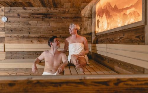 a man and woman sitting in a sauna at FOR MOMENTS Apartments & Spa in Roßhaupten