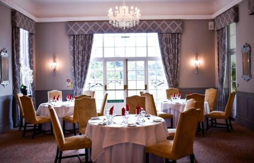 a dining room with tables and chairs and a chandelier at Dovecliff Hall Hotel in Burton upon Trent