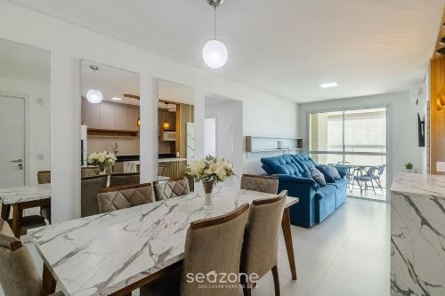a dining room and living room with a table and a blue couch at Condomínio a beira-mar c/ piscina - SHC in Piçarras