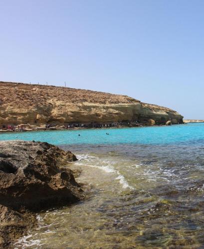 a beach with blue water and a hill in the background at Ageeba Beach Challet 17 in Marsa Matruh